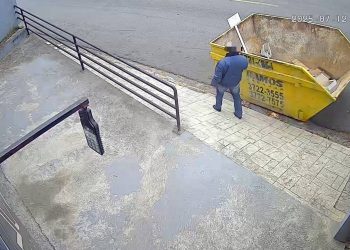 Homem retira placa de aviso e descarta entulho em caçamba alugada por empresa